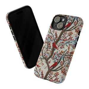 May include: A white phone case with a wintery design featuring red cardinals perched on branches with red berries. The case has a raised, textured design and a black camera lens cutout.