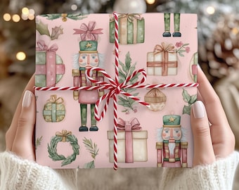 May include: A wrapped gift with pink wrapping paper featuring watercolor illustrations of nutcrackers, presents, and greenery. The gift is tied with red and white twine. The background is blurred, suggesting a festive holiday theme.