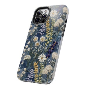 Op de afbeelding: Een blauwe telefoonhoes met een geborduurd bloemenpatroon met witte madeliefjes, paarse bloemen en groene bladeren.