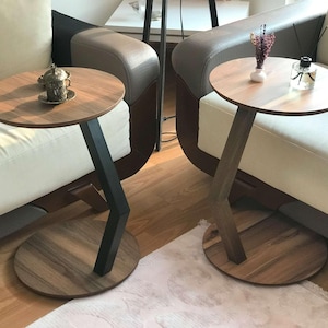 May include: Two wooden side tables with black metal legs. The tables have round tops and are placed next to two white couches.