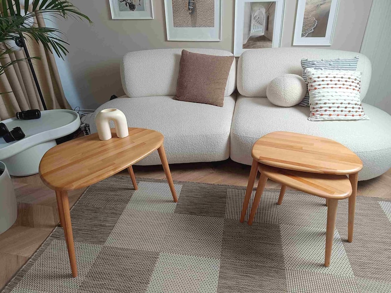 Two wooden oval-shaped coffee tables with a natural wood finish. The tables are nested together and are sitting on a patterned rug.