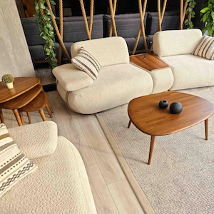 Two white fabric sofas with throw pillows, a wooden coffee table with two black decorative spheres, and a set of three nested wooden coffee tables. The furniture is arranged on a light beige rug.