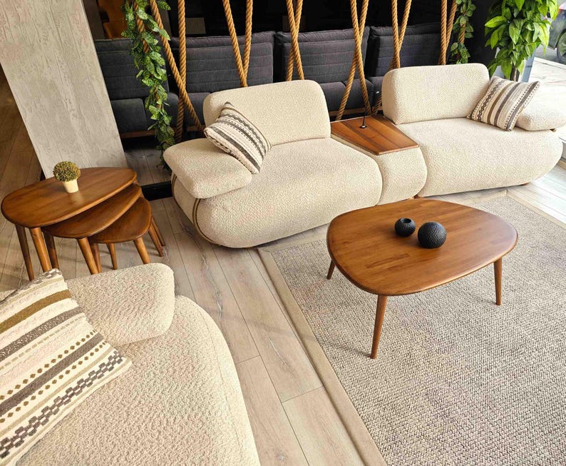 Two white fabric sofas with throw pillows, a wooden coffee table with two black decorative spheres, and a set of three nested wooden coffee tables. The furniture is arranged on a light beige rug.