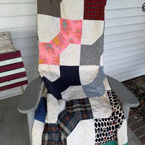 May include: A patchwork quilt featuring a variety of fabric squares in solid colors, plaid patterns, floral prints, and geometric designs. The quilt is constructed with white fabric blocks interspersed between the patterned pieces and a green border.
