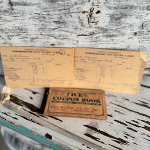 May include: Two vintage paper documents, one labeled "Purdue University Commercial Egg Score Card" and the other a "$1.00 Ice Coupon Book" from Earlington Ice Co. The items are on a weathered, white and teal painted wooden surface.