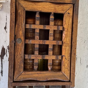 May include: A vintage wooden spice rack with glass jars. The rack has a small cabinet with a latticed door and shelves for the jars. The jars have labels that read "The Himark Of Taste".