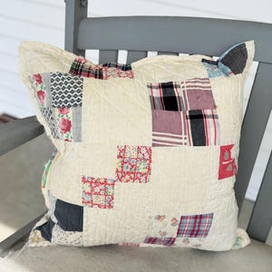 Puede incluir: Una almohada de patchwork con fondo blanco y cuadrados de varios patrones florales y a cuadros en tonos de rosa, rojo, azul y negro.
