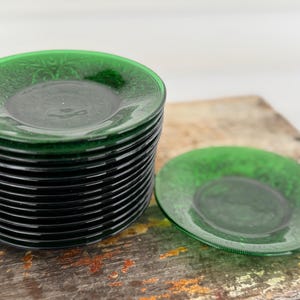 May include: A stack of green glass plates with a floral design. One plate is separate from the stack. The plates are on a wooden surface. The plates are approximately 6 inches in diameter.