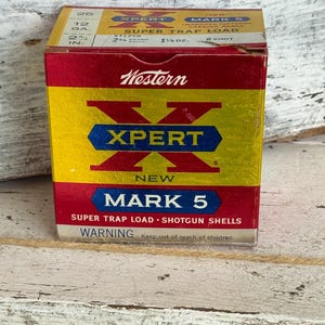 May include: A vintage box of Western Xpert Mark 5 shotgun shells. The box is red, yellow, and blue with the text "XPERT" and "MARK 5". The box also has the text "SUPER TRAP LOAD" and "WARNING".