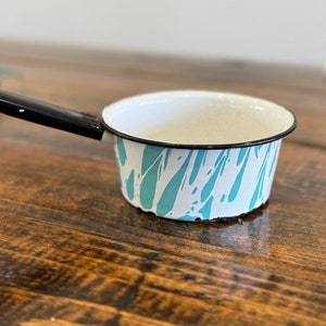 May include: A small white enamel saucepan with a black handle and a teal and white marbled design.