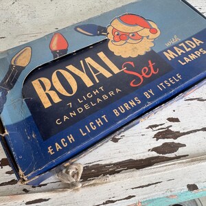 May include: Vintage Royal Set 7 Light Candelabra box with Mazda lamps. The blue box features a Santa Claus illustration and text. The box reads "Each light burns by itself".