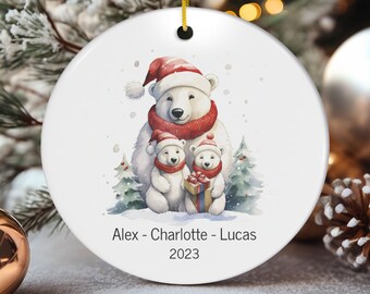 Puede incluir: Adorno navideño de cerámica blanca con una familia de tres osos polares. El oso padre lleva un gorro de Papá Noel rojo y una bufanda. Los dos cachorros llevan gorros de Papá Noel rojos. El adorno está personalizado con los nombres "Alex - Charlotte - Lucas" y el año "2023".