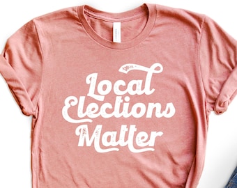 May include: A pink t-shirt with the text "Local Elections Matter" in white retro-style lettering.
