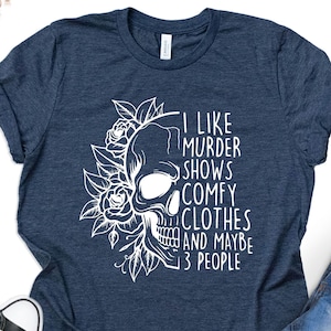 May include: A navy blue t-shirt with a white skull and floral design. The text on the shirt reads "I like murder shows comfy clothes and maybe 3 people".