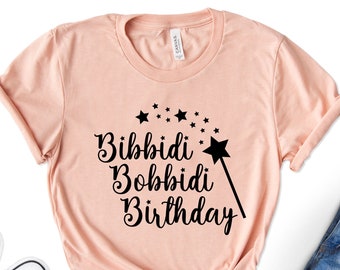 May include: A peach-colored t-shirt with a black graphic that says "Bibbidi Bobbidi Birthday" with a wand and stars.