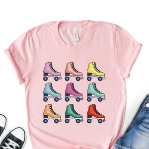 May include: Pink t-shirt with a graphic of nine colorful roller skates on a white background.