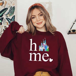 Puede incluir: Sudadera color burdeos con un gr&aacute;fico blanco de un castillo y el texto "home" y "me" con un peque&ntilde;o icono de Mickey Mouse.