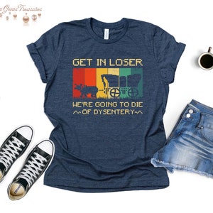 Op de afbeelding: Een marineblauw t-shirt met een vintage-stijl grafische afbeelding van een wagen en de tekst "GET IN LOSER WE'RE GOING TO DIE ~OF DYSENTERY~~"