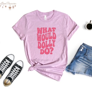 May include: A pink t-shirt with the text "What Would Dolly Do?" in pink retro-style lettering.