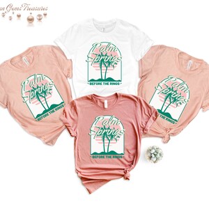 May include: Three t-shirts with a pink and green graphic design that says "Palm Springs" with palm trees and a sunset. The text below the graphic says "Before the Rings".