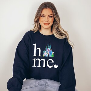 Puede incluir: Una sudadera azul marino con un gr&aacute;fico blanco de un castillo y el texto "home" y "me" con un peque&ntilde;o icono de Mickey Mouse.