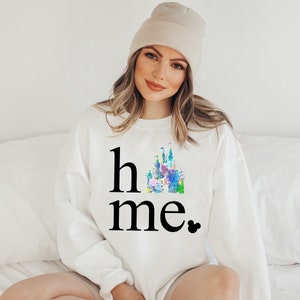 Puede incluir: Sudadera blanca con un gr&aacute;fico negro de un castillo de acuarela y el texto "home" con una cabeza de Mickey Mouse negra.