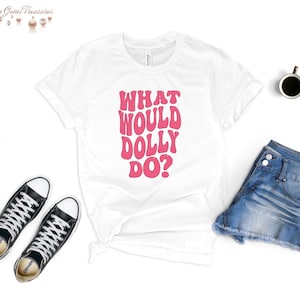 May include: White t-shirt with pink text that reads "What Would Dolly Do?" in a retro font.