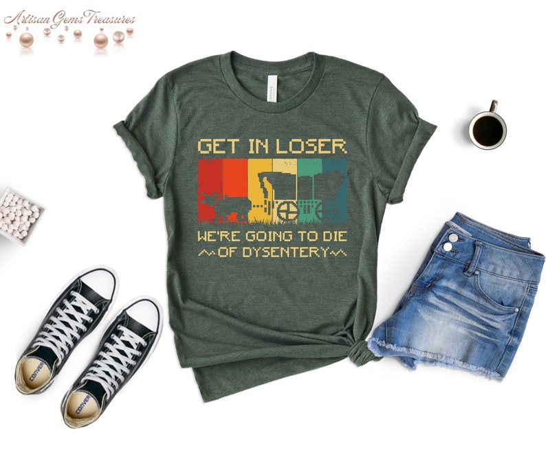 Op de afbeelding: Groen T-shirt met een vintage-stijl grafische afbeelding van een wagen en de tekst "GET IN LOSER. WE'RE GOING TO DIE ~OF DYSENTERY~"