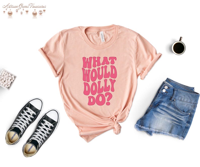 May include: A peach-colored t-shirt with the text "What Would Dolly Do?" in pink lettering. The text is in a retro font style.