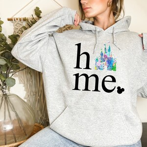 Puede incluir: Sudadera gris con una ilustraci&oacute;n de acuarela de un castillo y el texto "home" con un icono de Mickey Mouse.