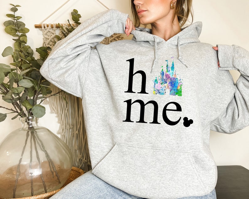 Puede incluir: Sudadera gris con una ilustraci&oacute;n de acuarela de un castillo y el texto "home" con un icono de Mickey Mouse.