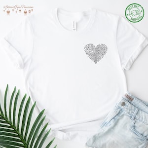 May include: White t-shirt with a black circuit board heart design. The shirt has a crew neck and short sleeves. The design is on the left chest area. The shirt is paired with denim shorts. The image also includes a green plant and the text "Next Day Shipping".