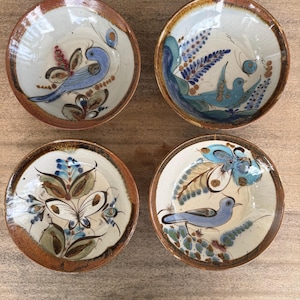 May include: Four round ceramic bowls with a cream-colored interior and a brown rim. Each bowl features hand-painted designs including blue birds, butterflies, and floral motifs in shades of blue, green, and brown on the interior surface.