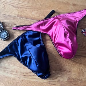 May include: Two pairs of satin underwear, one pink and one navy blue. The underwear is laid out on a wooden surface.