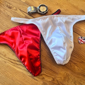 May include: Two pairs of satin underwear, one red and one white, with black trim. The underwear is laid out on a wooden surface.