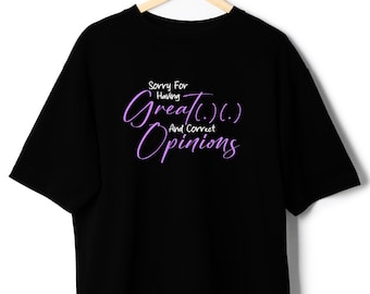 May include: Black t-shirt with the text "Sorry For Having Great And Correct Opinions" in a cursive, purple font. The shirt is hanging on a wooden hanger against a white background. The t-shirt has short sleeves.