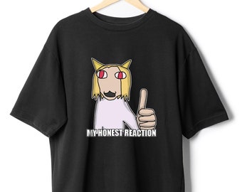 May include: Black t-shirt with a cartoon illustration of a person with yellow hair and red eyes giving a thumbs up. The text "MY HONEST REACTION" is printed below the illustration.
