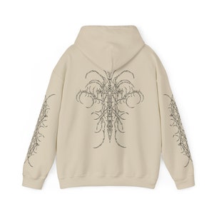 Pu&ograve; includere: Una felpa con cappuccio beige con una stampa grafica in bianco e nero di una croce con dettagli intricati sul retro e sulle maniche.