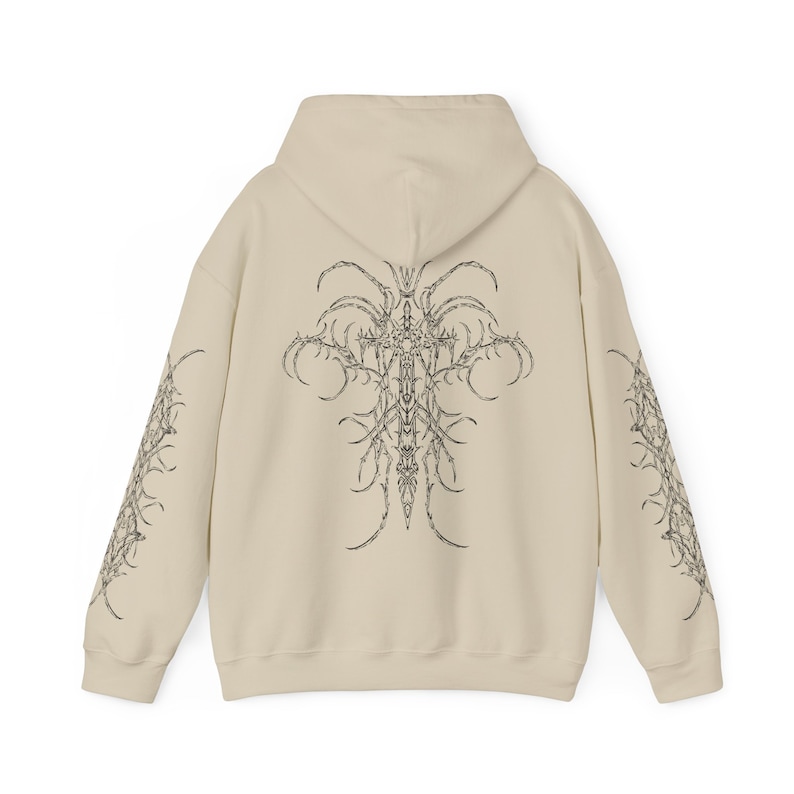 Pu&ograve; includere: Una felpa con cappuccio beige con una stampa grafica in bianco e nero di una croce con dettagli intricati sul retro e sulle maniche.
