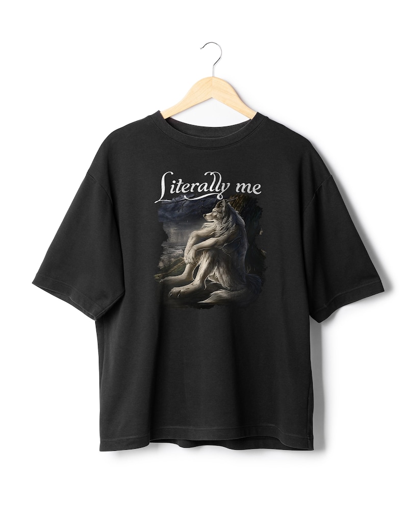 May include: Black t-shirt featuring a detailed graphic of a wolf embracing itself, set against a landscape with a dark sky. The words "Literally me" are written in white script above the image. The shirt has short sleeves and a crew neck.