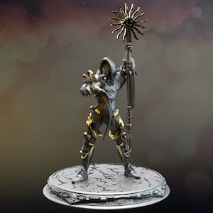 Può includere: Una statuetta in argento e oro di una figura incappucciata che tiene uno scettro con un designo a forma di sole. La figura indossa un'armatura e un mantello. La figura è in piedi su una base circolare con un design di pietra screpolata.
