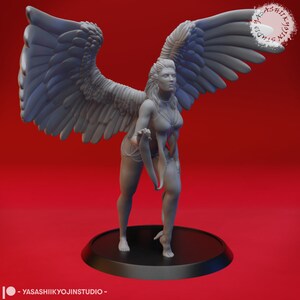 May include: A grey, detailed figurine of a winged woman with outstretched wings. She is wearing a flowing garment and holding a ribbon in her hand. The figurine is standing on a black circular base.