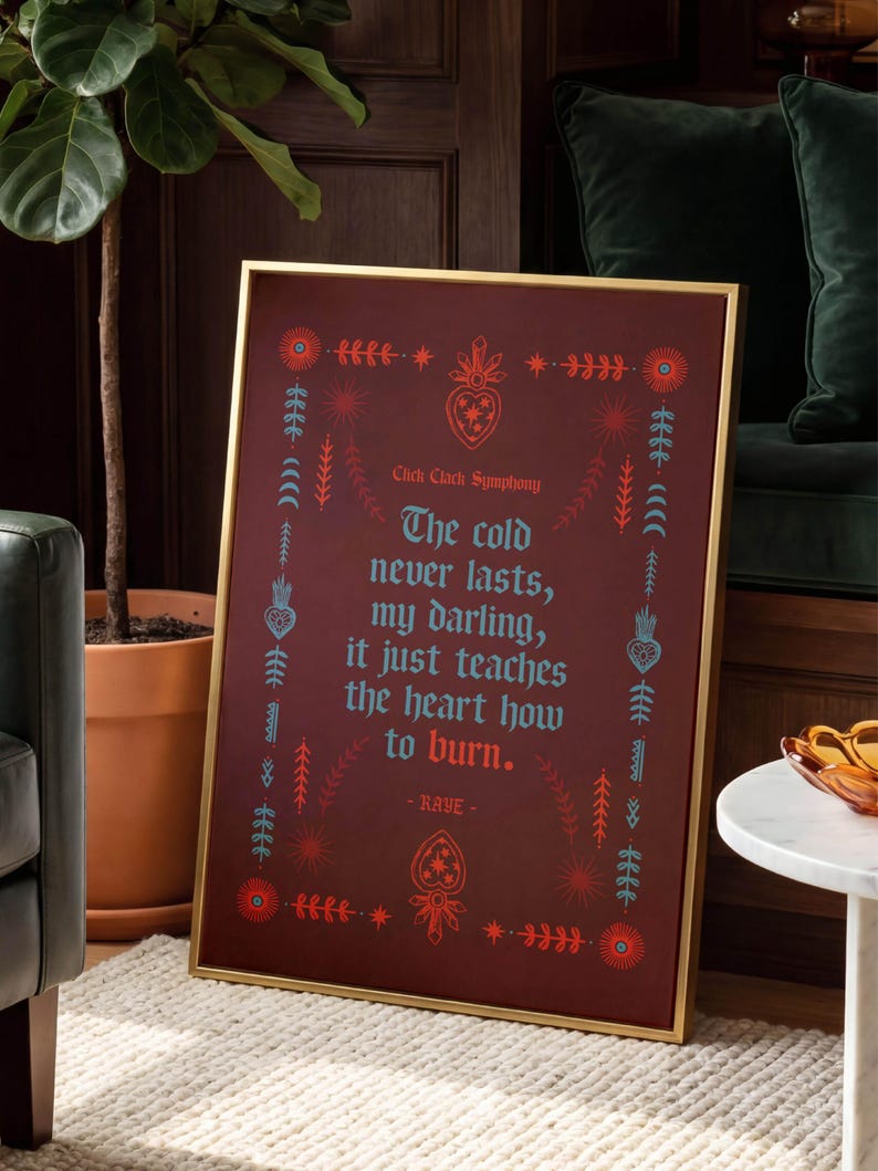 May include: A framed art print with a gold frame. The print has a burgundy background with teal and red decorative elements and text that reads "The cold never lasts, my darling, it just teaches the heart how to burn."