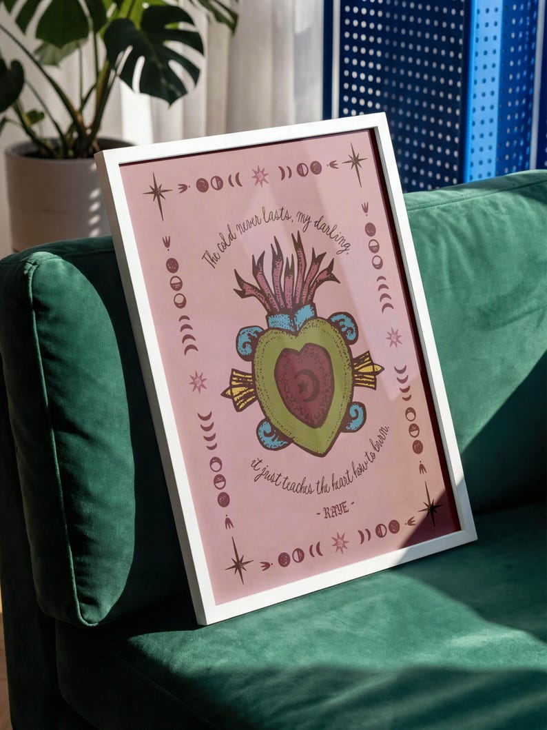 May include: A framed art print with a white border, featuring a pink background and a central illustration of a heart-shaped design with text. The artwork includes celestial and botanical elements, with the quote "The old never lasts, my darling, it just teaches the heart how to burn."