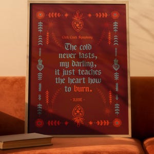 May include: Framed art print with a burgundy background and decorative floral and geometric elements. The text reads "The cold never lasts, my darling, it just teaches the heart how to burn." by RAYE.