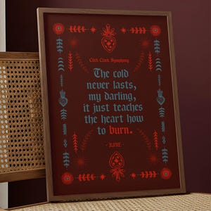 May include: Framed art print with a dark red background and a wooden frame. The print features decorative floral and heart motifs in red and teal, surrounding the quote "The cold never lasts, my darling, it just teaches the heart how to burn."