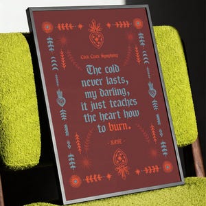 May include: Framed art print with a burgundy background and decorative floral and star motifs. The text reads "The cold never lasts, my darling, it just teaches the heart how to burn." The artist is RAYE.