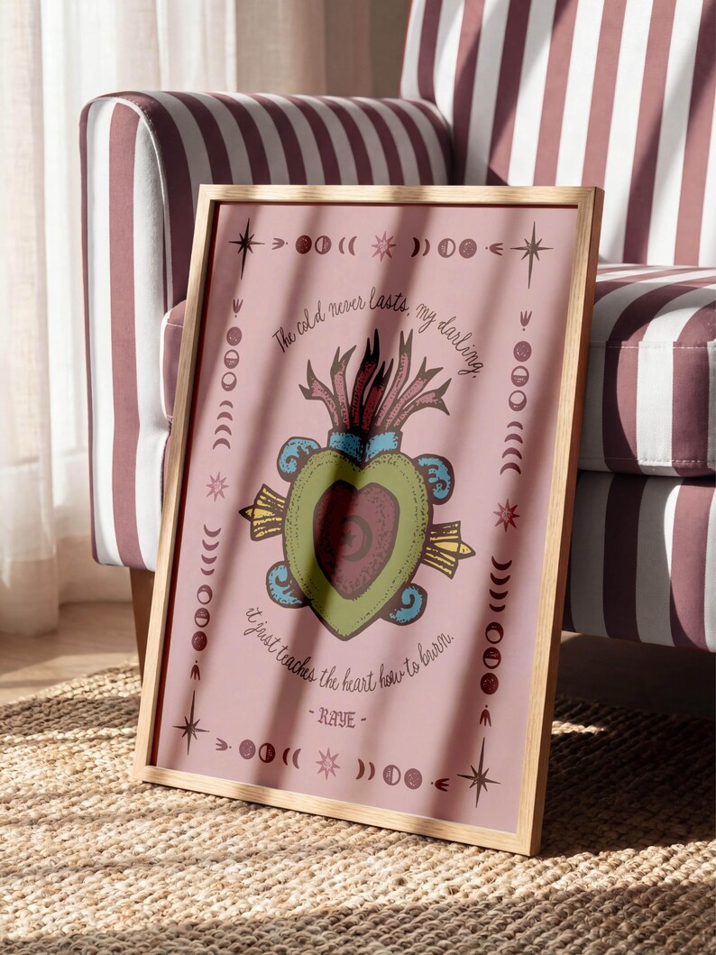 May include: A framed print with a pink background features a heart-shaped design with a red and green color scheme. The text "The cold never lasts, my darling. It just teaches the heart how to burn. - RAYE-" is written around the design. The frame is made of wood.
