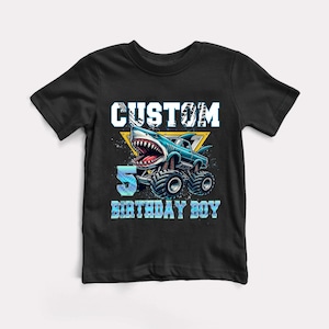 May include: Black t-shirt with a blue monster truck with a shark head and the text "CUSTOM 5 BIRTHDAY BOY" in white.
