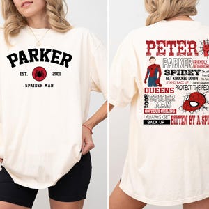 May include: A white t-shirt with a red spider graphic and the text "Parker Est. 2001 Spaider Man" on the front. The back of the shirt has a red spider graphic and the text "Peter Parker Friendly Neighborhood Spidey Get Knocked Down Stand Back Up Queens 2001 Spider Man On Your Ceiling I Always Get Bitten By A Spider Back Up".